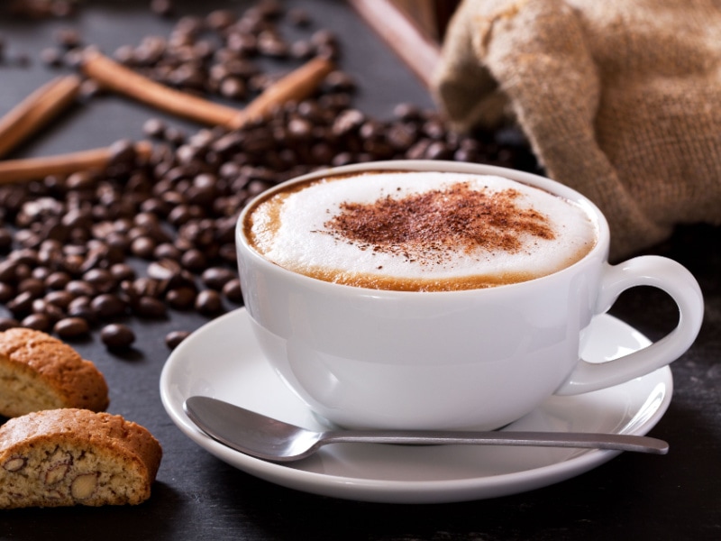 A Cup of Cappuccino with Coffee Beans and Bread on Background