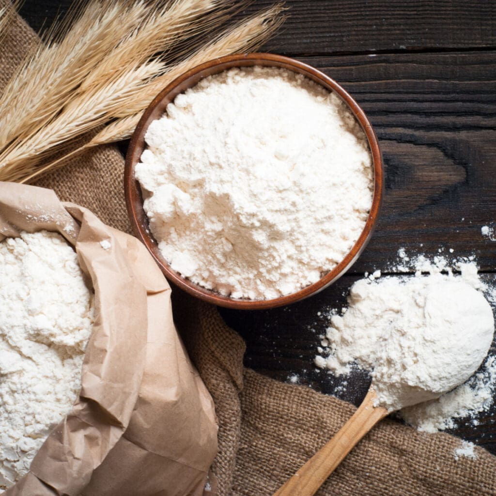 How to Make Self-Rising Flour: Flour in a Bowl and Bag of Flour on a Wooden Table with Wheat Stalks and a Wooden Spoon
