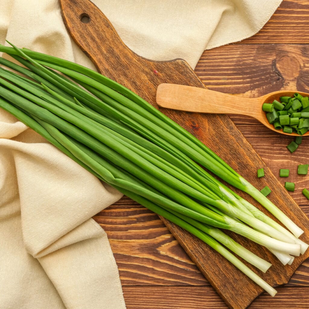 How to Store Green Onions featuring Green Onions on Wooden Cutting Board And Chopped Onions on the Side