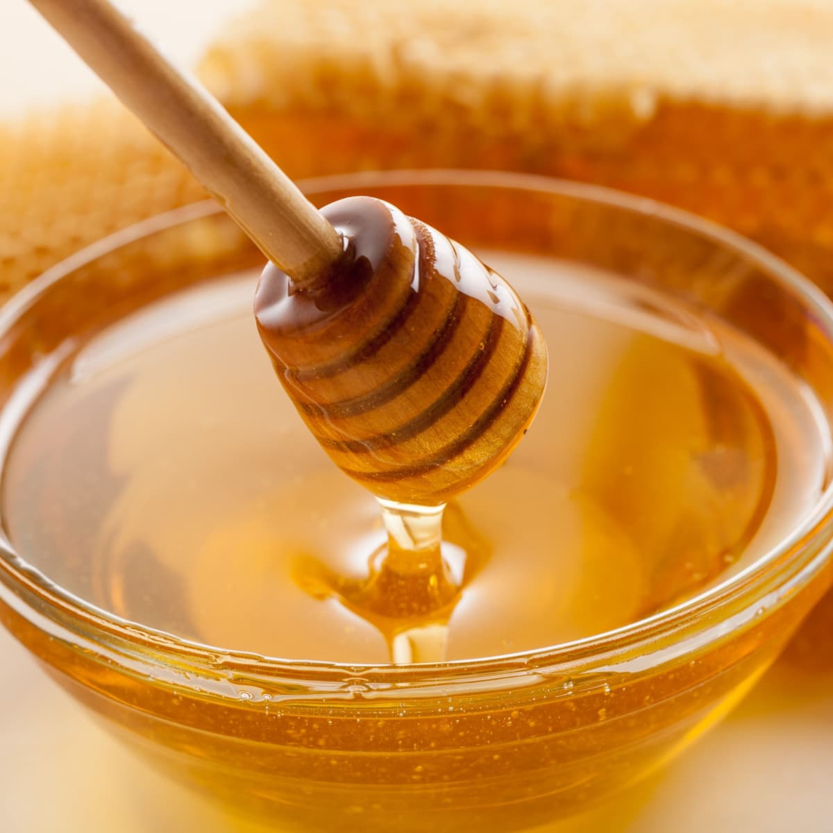 How to Soften Honey- 4 Best Ways featuring Honey Dipper Coming Out of a Small Glass Bowl of Honey