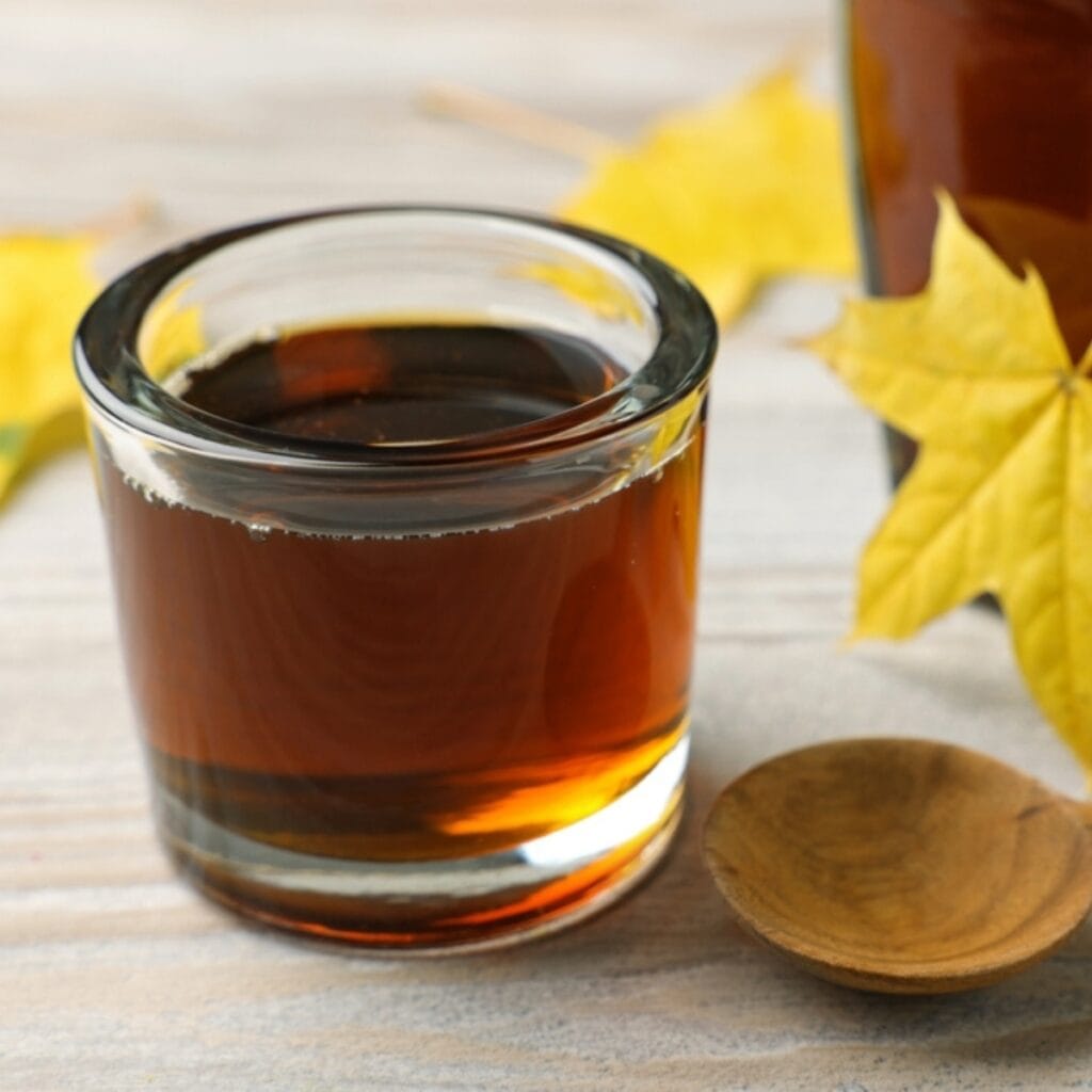 Maple Syrup in a Small Glass Jar with Maple Leaves in the Background