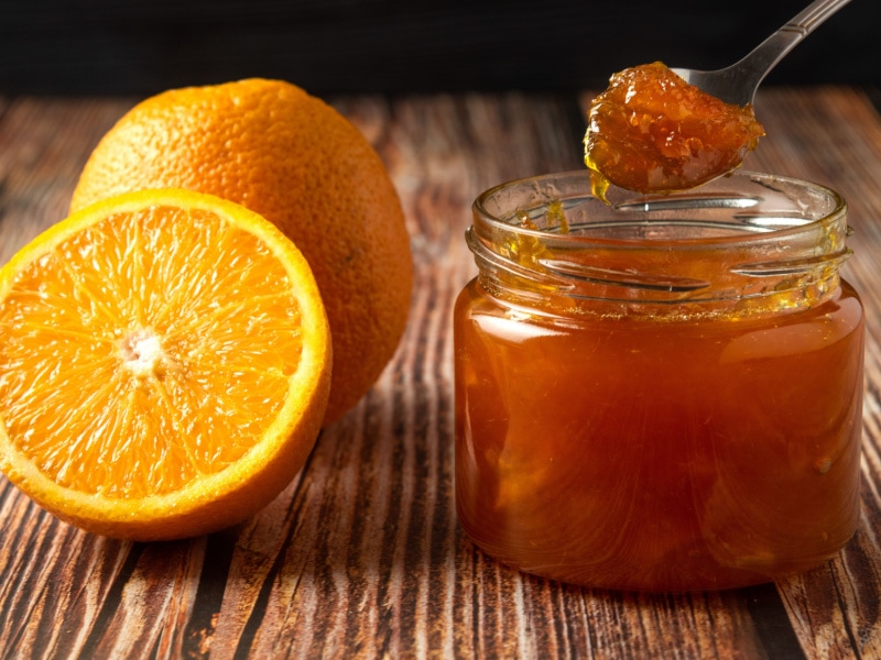 A Jar of Orange Marmalade and Slices of Oranges on a Wooden Table