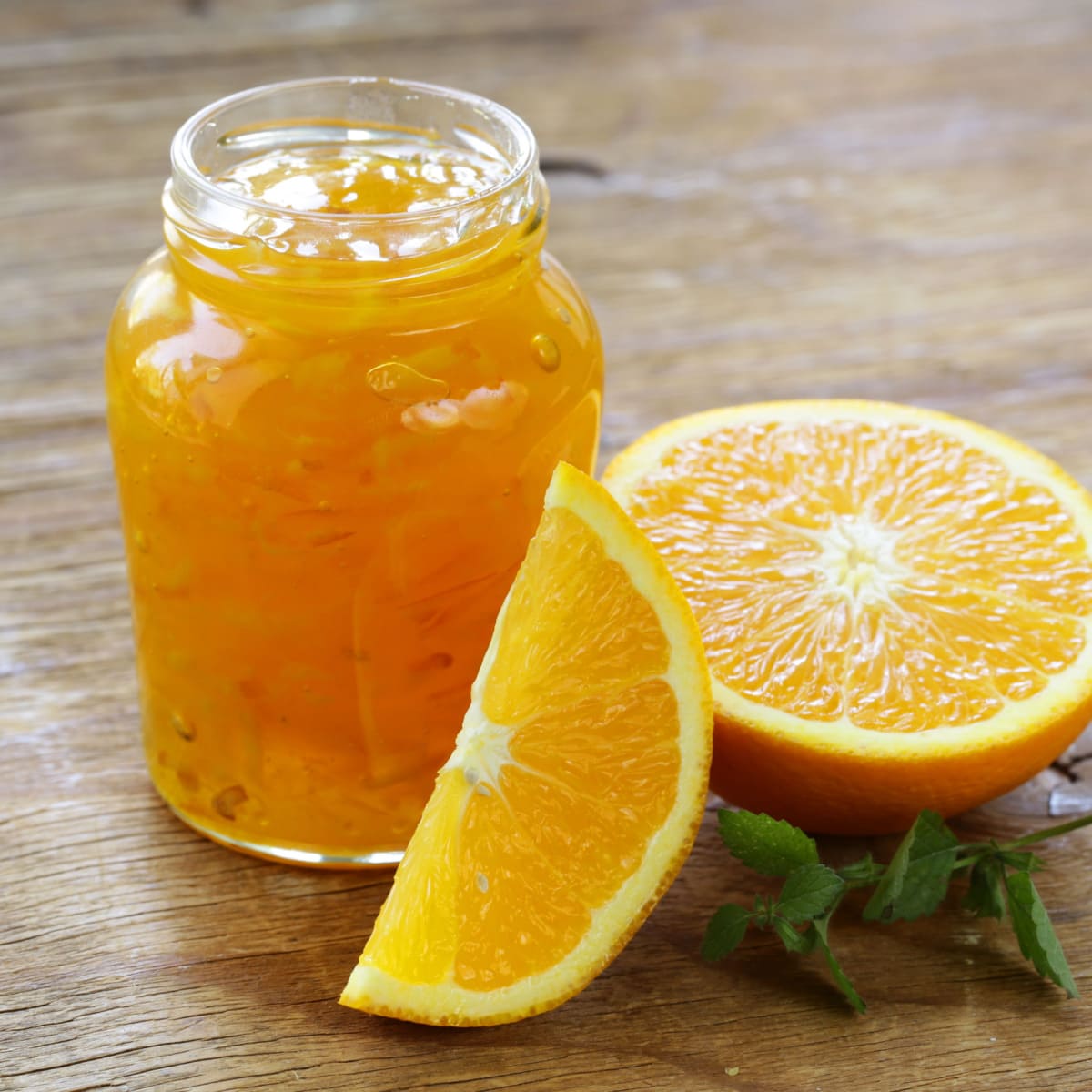 What Is Marmalade? (+ How to Make It) featuring A Jar of Orange Marmalade and Sliced Orange on a Wooden Table