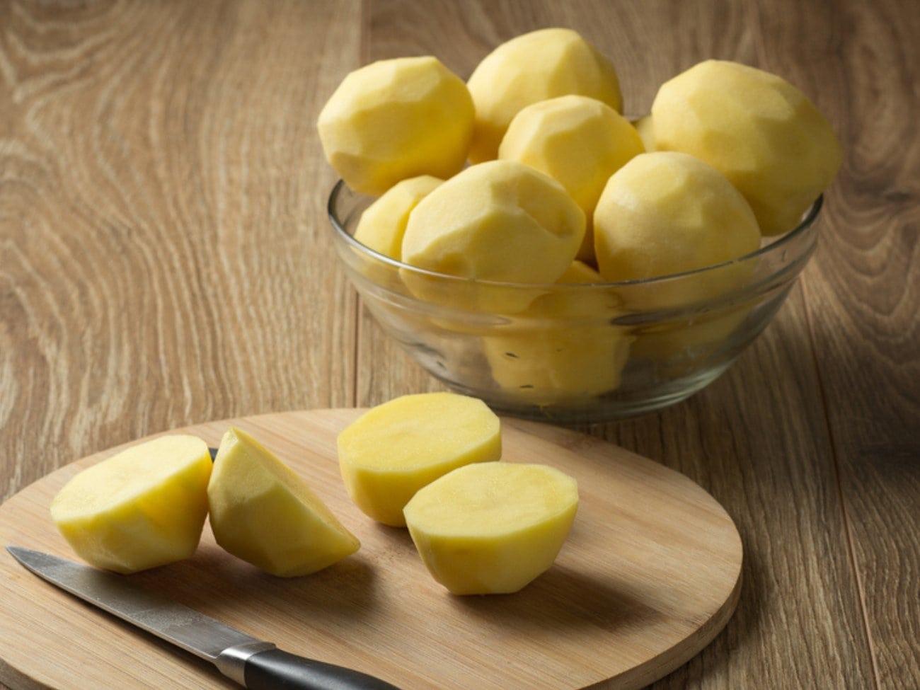 Peeled Potatoes in a Glass Bowl, Two Potatoes Cut in Half on a Wooden Chopping Board