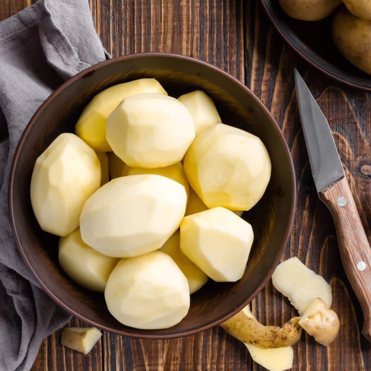 How to Keep Potatoes From Turning Brown featuring Peeled Potatoes in a Bowl on a Wooden Table with a Pairing Knife Next To It