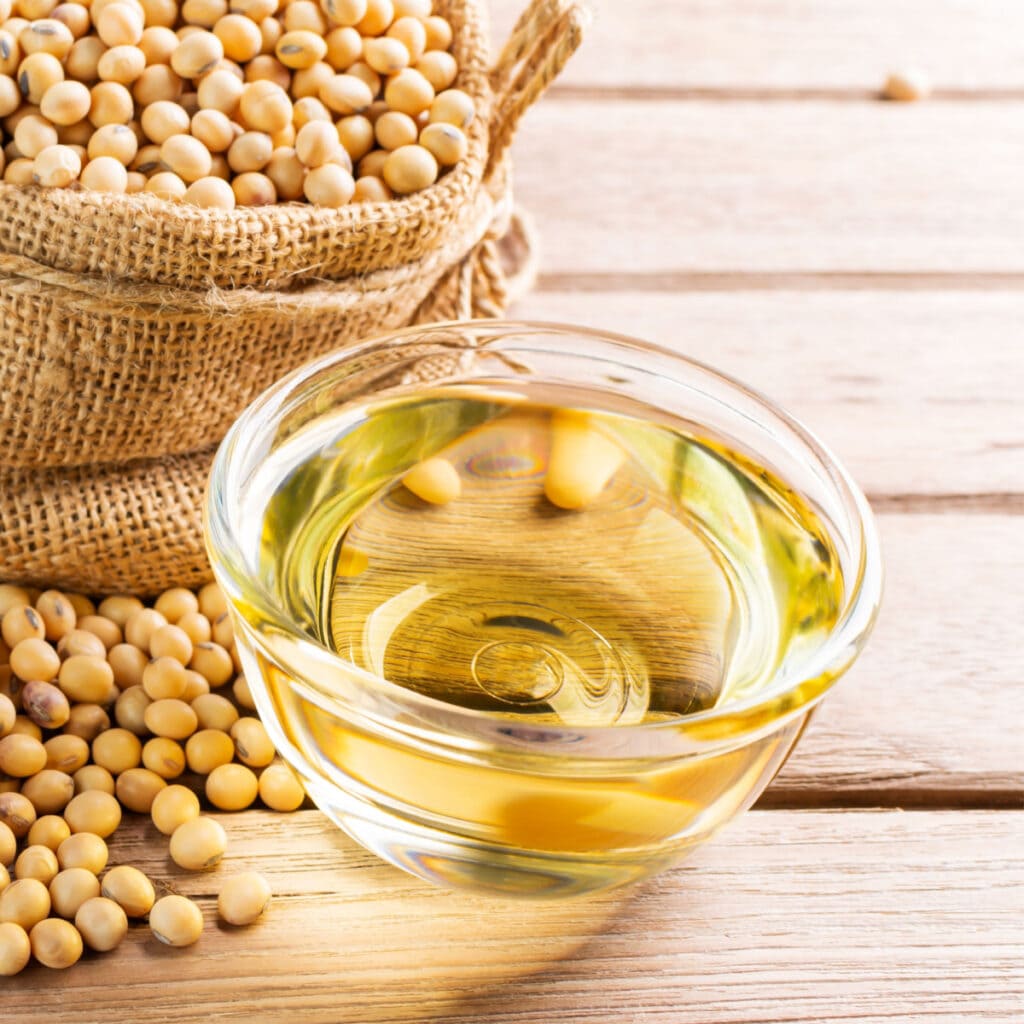 A Bowl of Soybean Oil and A Bag of Soybeans on a Wooden Table