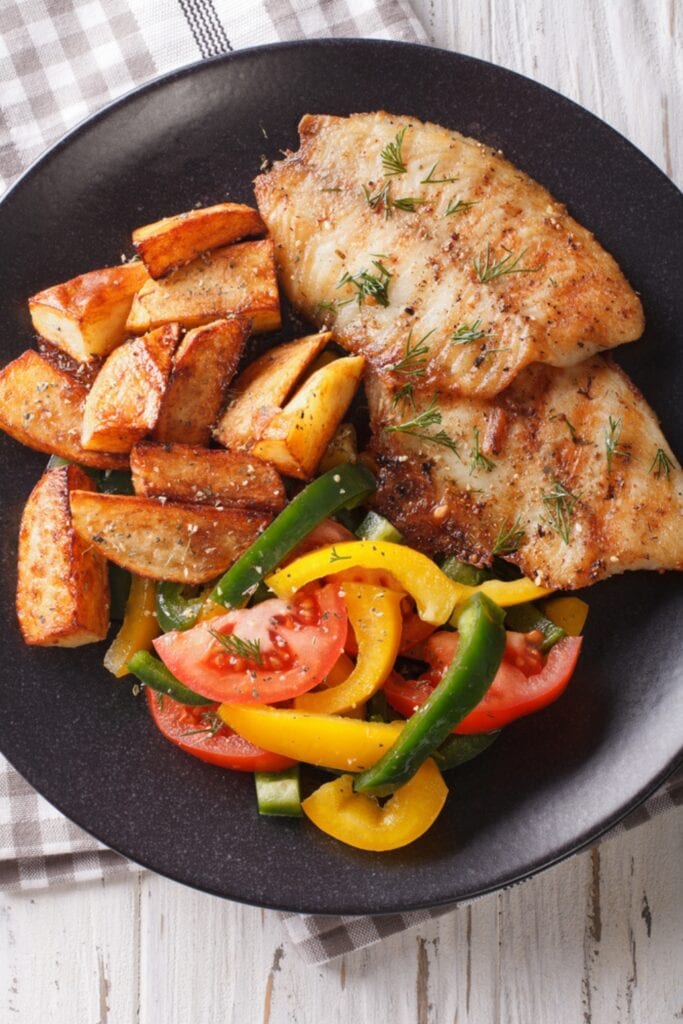 Oven Baked Tilapia Fillet Seasoned and Served With Fresh Vegetables and Fried Potatoes