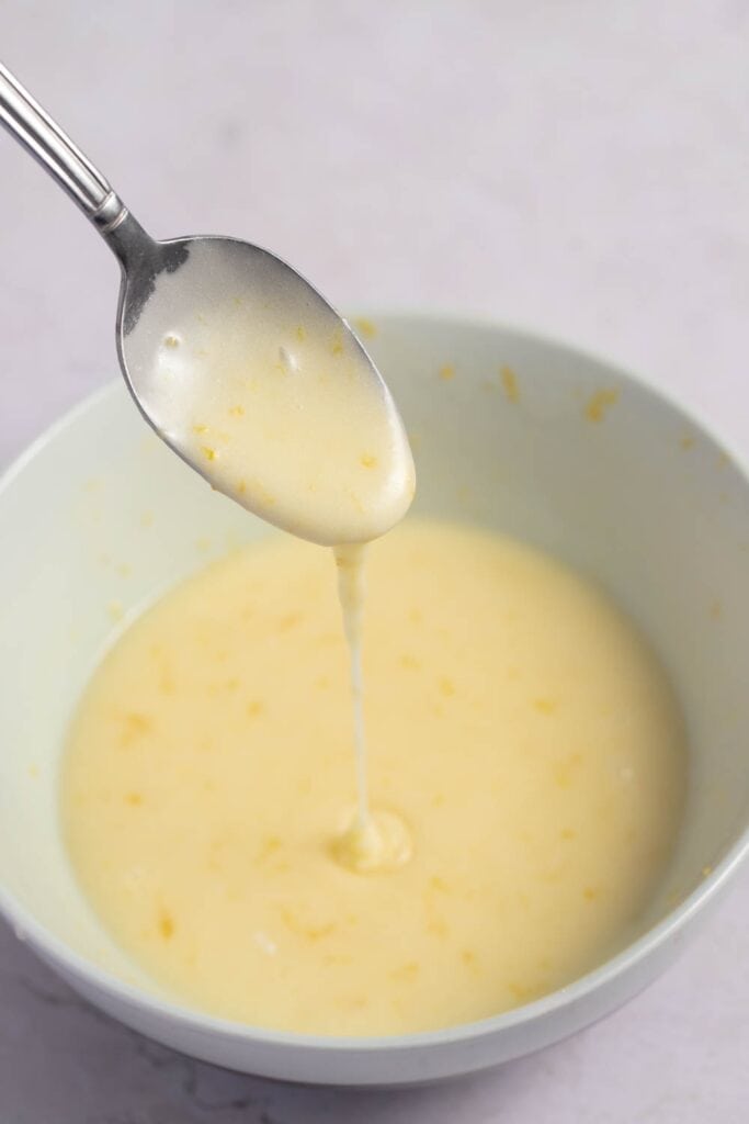 Orange Glaze Icing Dripping From a Spoon into a Bowl of Orange Glaze Icing