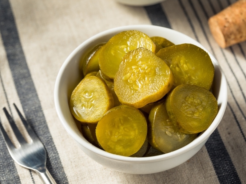Green Bread and Butter Pickle Chips in a Bowl on a Striped Table Cloth
