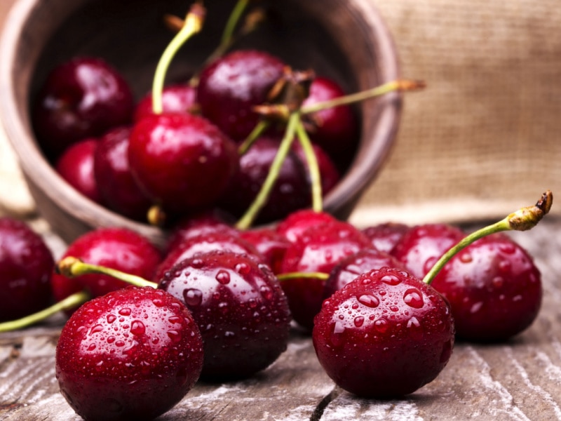 Bunch of Fresh Wet Cherries on a Wooden Table with More in a Bowl in the Background