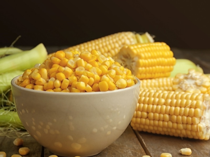 A Bowl of Corn Kernels and Whole Corn on a Wooden Table