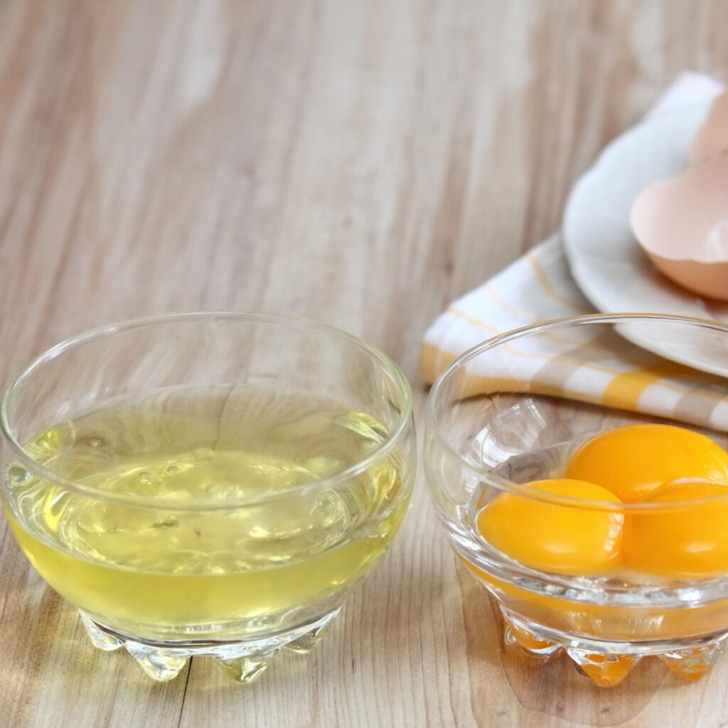Separated Egg Whites and Yolks into Two Glass Bowls on a Wooden Table