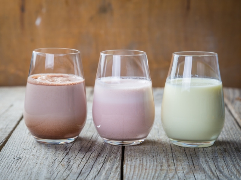 Three Glasses of Flavored Milk in Chocolate, Strawberry, and Vanilla on a Wooden Table