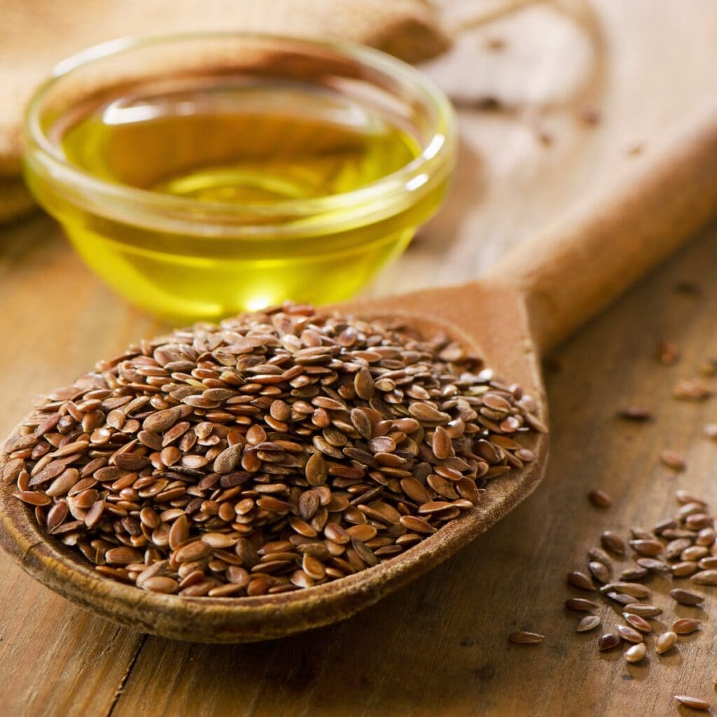 Flax Seeds on a Wooden Spoon with a Small Glass Bowl of Oil in Background
