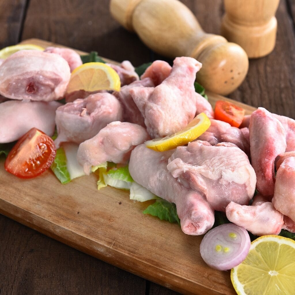 How to Defrost Chicken Safely (3 Ways): Frozen Chicken on a Wooden Board with Tomatoes and Lemon