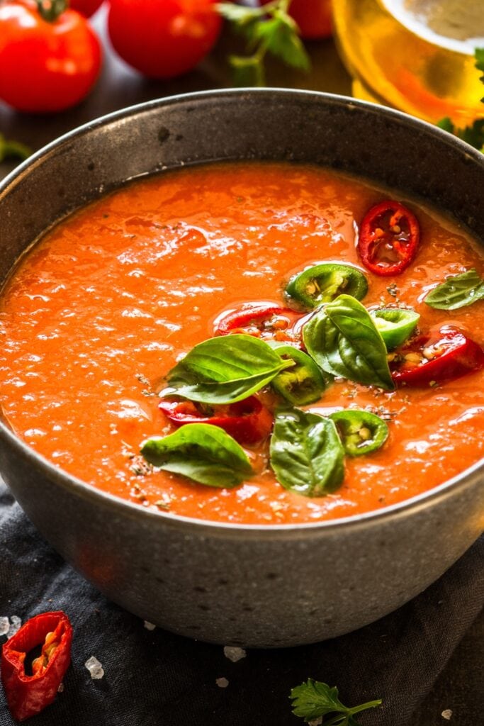 What to Serve with Gazpacho featuring Gazpacho Tomato Soup in Large Brown Bowl with Chili Peppers and Basil