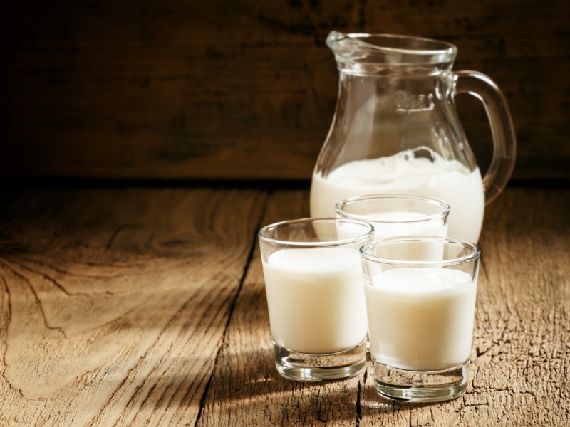 Fresh Goat Milk in a Glass Pitcher and Three Drinking Glasses on a Wooden Table