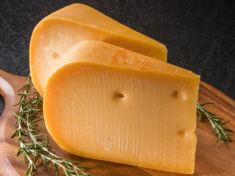 Two Chunk Slices of Gouda Cheese and Thyme Leaves on a Wooden Cutting Board