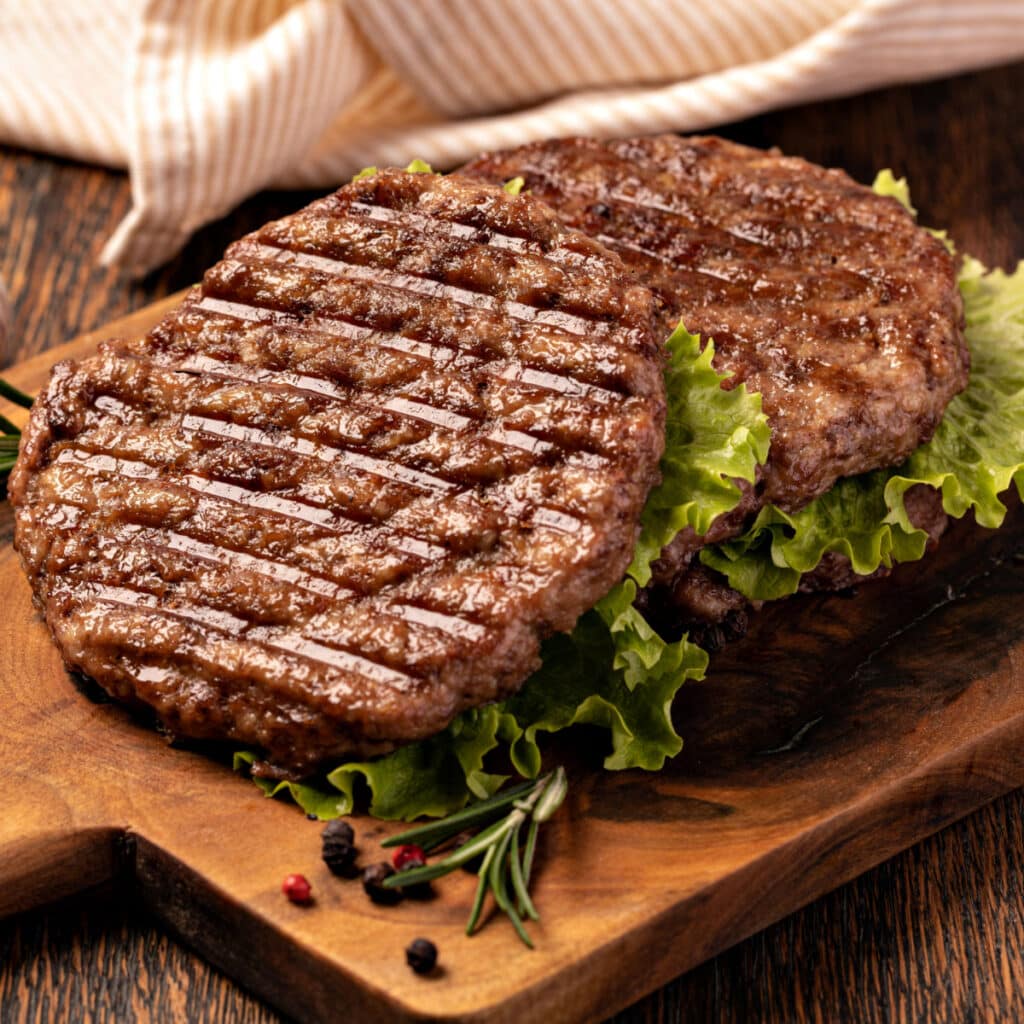 Best Ground Beef for Burgers (Tips & Tricks) featuring Freshly Grilled Ground Beef Patties with Lettuce on a Wooden Cutting Board
