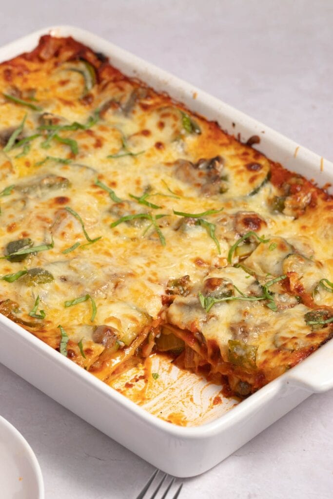 Healthy and Cheesy Vegetable Lasagna in a White Casserole Dish with One Slice Missing