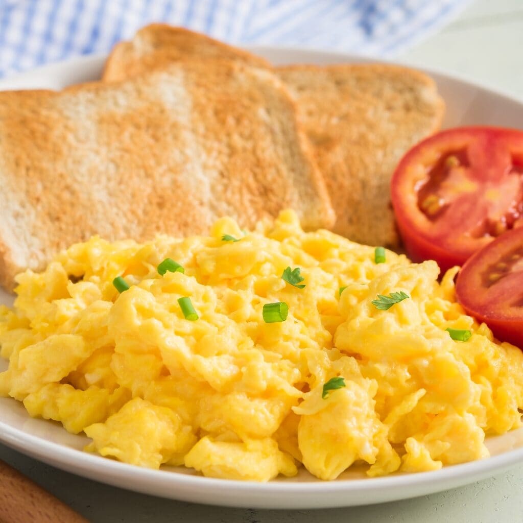 Homemade Scrambled Eggs with Bread and Tomatoes on a White Plate