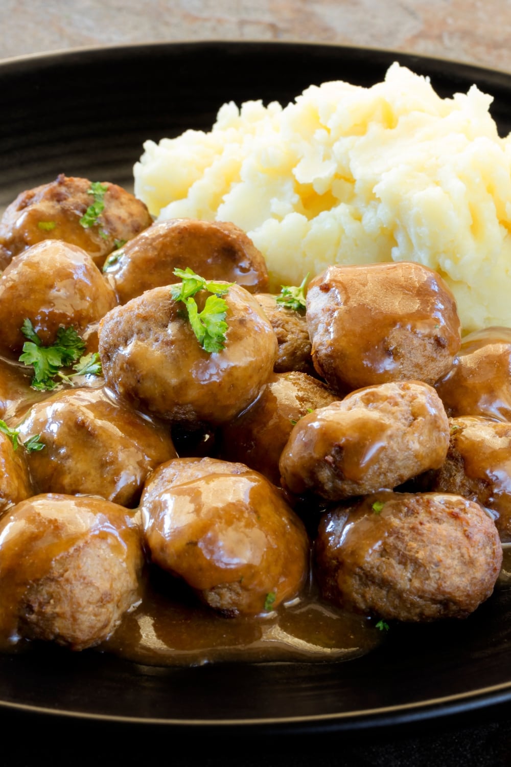 A plate of Swedish meatballs topped with gravy, with mashed potatoes on the side