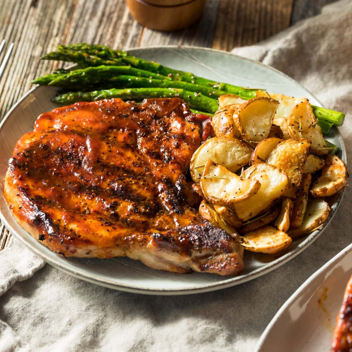 Honey Garlic Pork Chops Served on a Plate with Roasted Potatoes and Asparagus