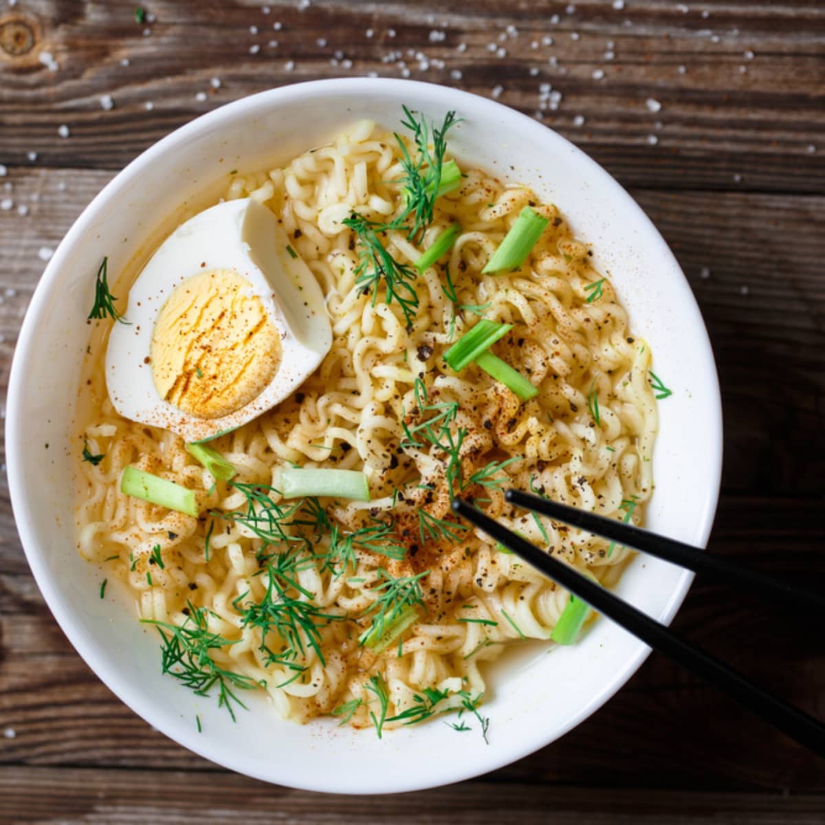 Bowl of Ramen Noodles With Boiled Eggs, Sliced Onions and Herbs and Chopsticks