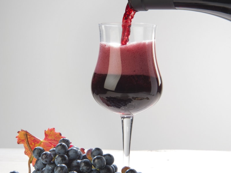 Bottle of Lambrusco Wine Pouring into a Glass with Grapes on The Table