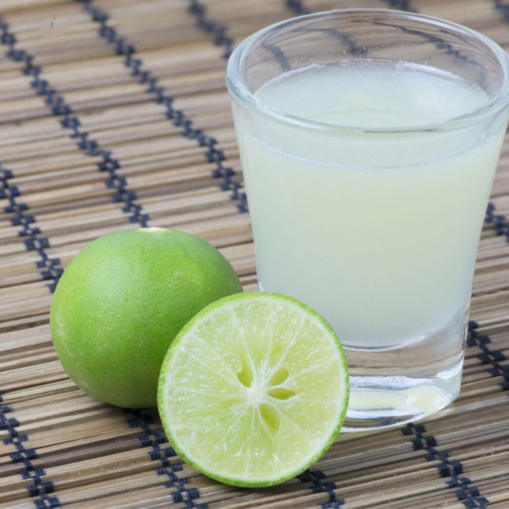 Glass of Fresh Lime Juice on a Bamboo Mat with One Sliced Lime and One Whole Lime to the Side