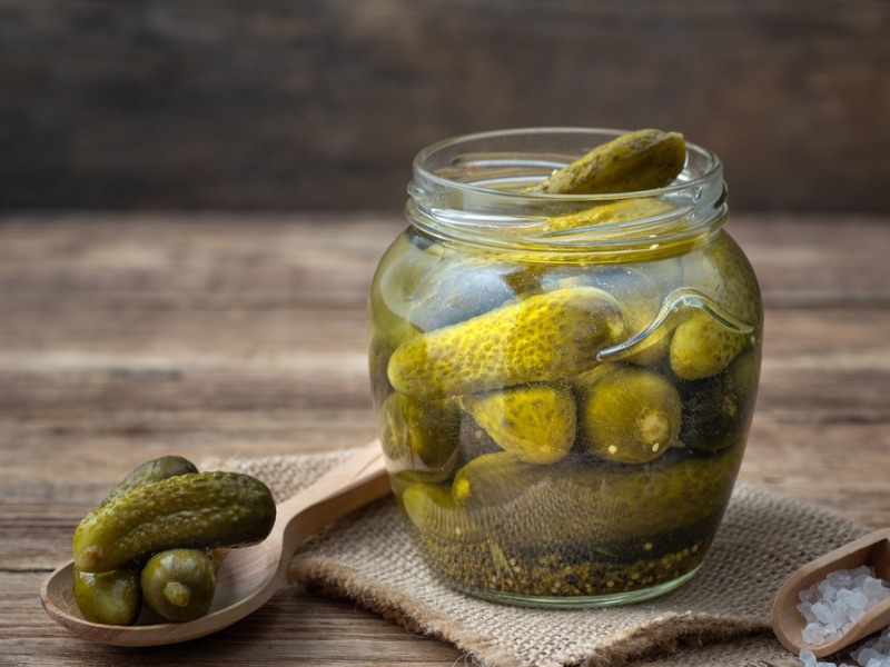 Lime Pickles in Glass Jar on a Wooden Table and Three Lime Pickles on a Wooden Spoon