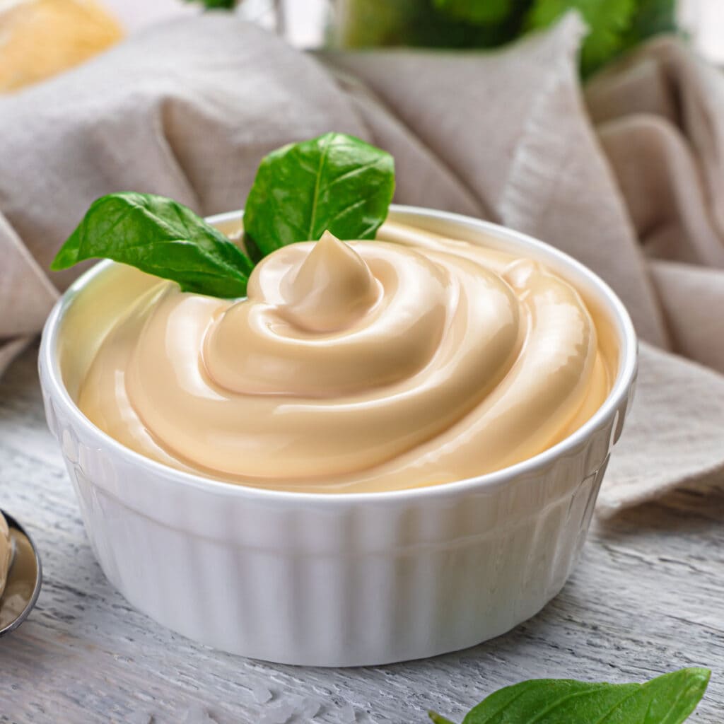 Miracle Whip vs. Mayo: What's the Difference? featuring A Bowl of Mayo on a Wooden Table with a Basil Garnish