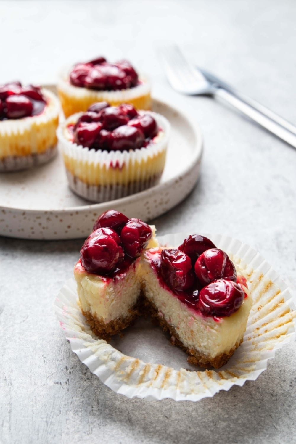 Mini Cheesecake with Cherries Sliced in Half and 3 Whole Mini Cheesecakes with Cherries in the Background
