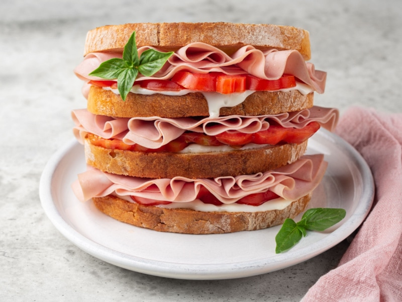Giant Mortadella Sandwich with Cheese, Tomatoes, Sauce, Basil, and Four Slices of Bread on a White Plate