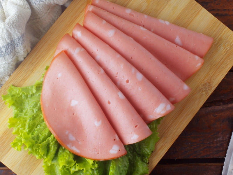 Slices of Mortadella on a Wooden Cutting Board, Garnished with Lettuce