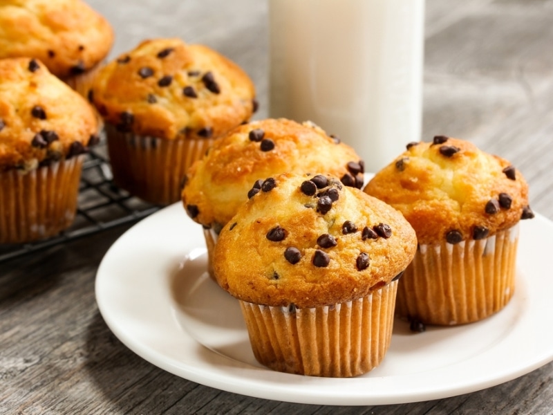 Freshly Baked Homemade Chocolate Chips Muffins on a Plate with More on a Cooling Rack in the Background Plus a Jar of Milk