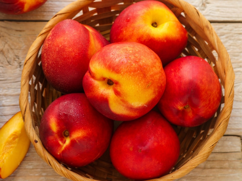 Bushel of Fresh Nectarines in a Woven Basket on a Wooden Table