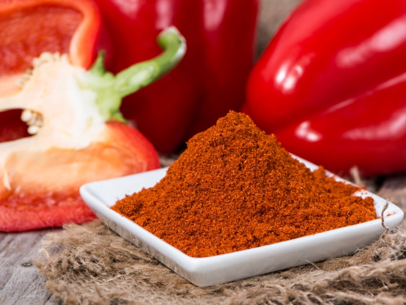 Paprika Powder on a Saucer and Bell Peppers on a Wooden Table