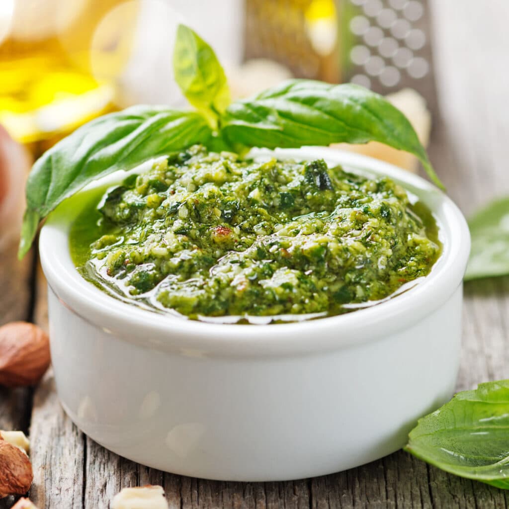 A Bowl of Pesto Sauce on a Wooden Table with Fresh Basil and Nuts 