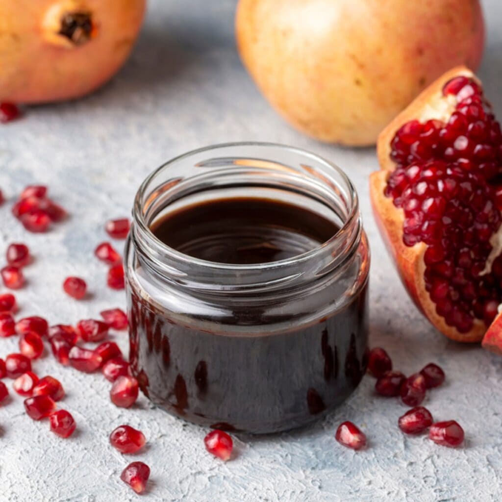 Small Jar of Pomegranate Syrup With Fresh Pomegranate and Seeds Scattered Around