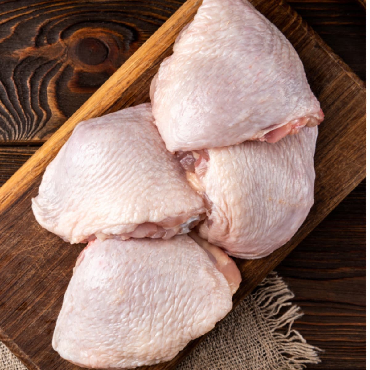 Raw  skin-on chicken thighs on a cutting board.