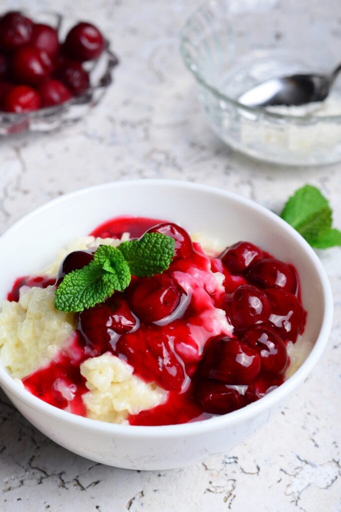25 Sour Cherry Recipes You'll Love featuring Rice Pudding with Cherry Sauce and Mint Sprig on a White Background