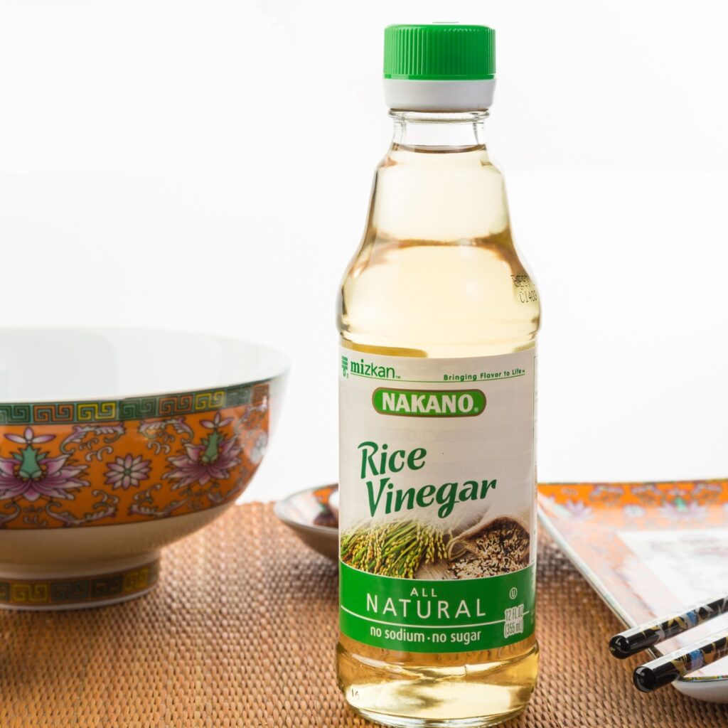 Bottle of Nakano Rice Vinegar on Bamboo Placemat With Asian-Designed Serving Dishes in Background and Decorative Chopsticks