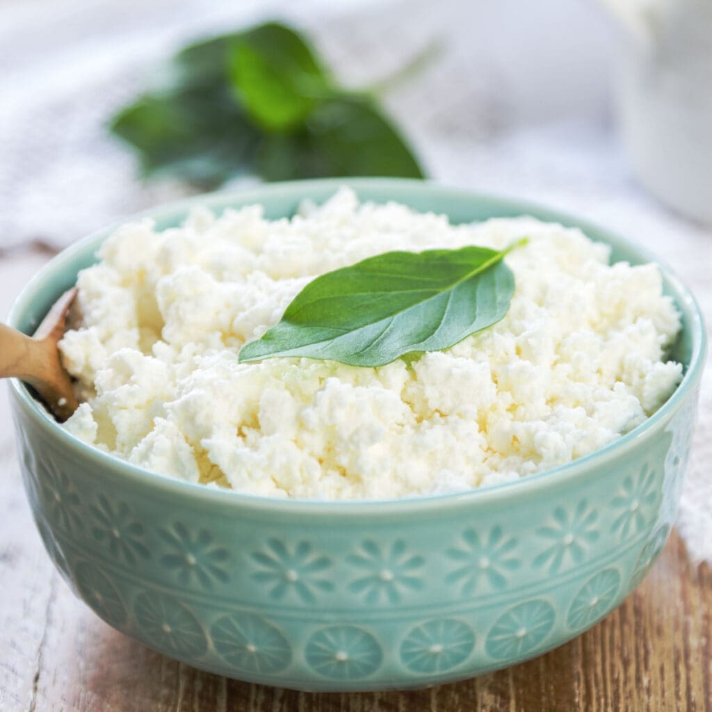 A Bowl of Ricotta Cheese with Mint Leaf on Top on a Wooden Table