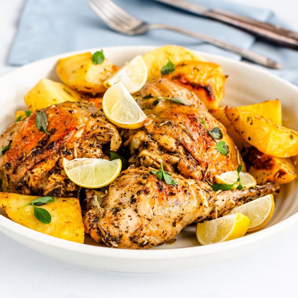 Greek-Style Baked Chicken Thighs Served with Greek Lemon Potatoes and Lemon Wedges
