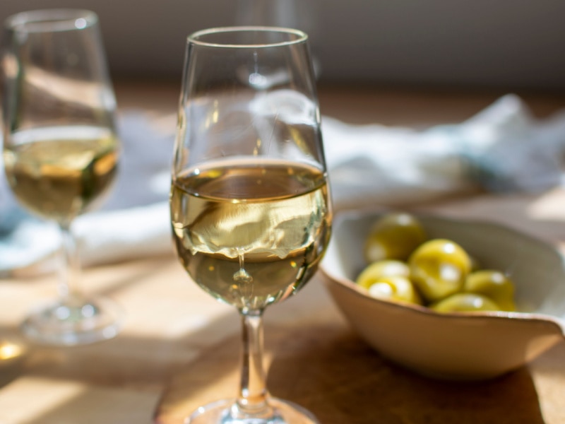 A Glass of Sherry Wine and a Bowl of Olives on a Wooden Table