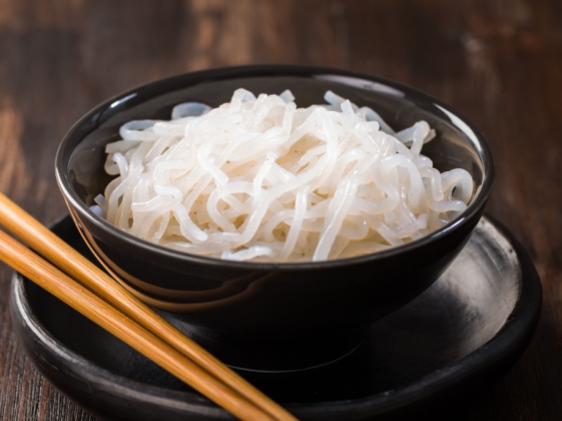 Plain Shiratake Noodles in a Black Bowl on a Black Plate with Wooden Chopsticks