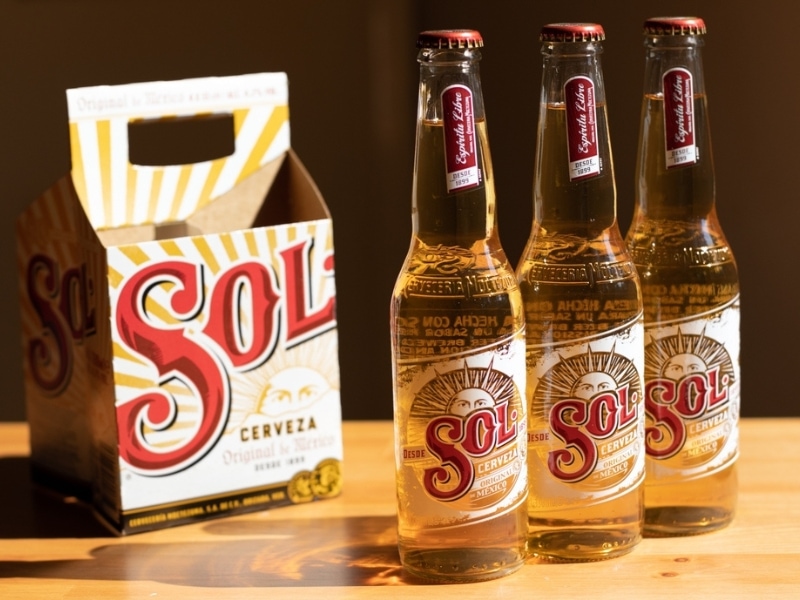 Three Sol Cerveza Bottles and Empty Sol Cerveza Carrier Box on a Table