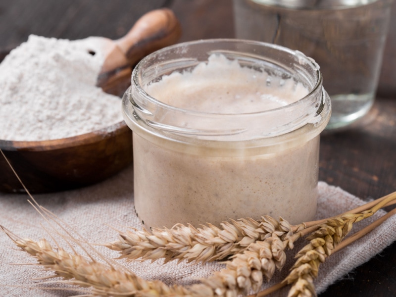 Glass Jar of Sourdough Starter and A Bowl of Wheat on a Wooden Table