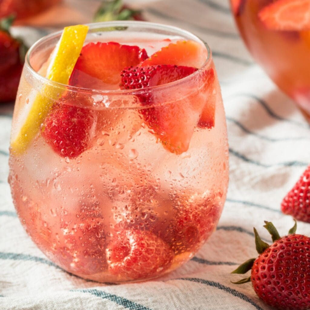 Glass of Ice Cold Strawberry Cocktail with Slices of Fresh Strawberries, Lemon Wedge, and Raspberries